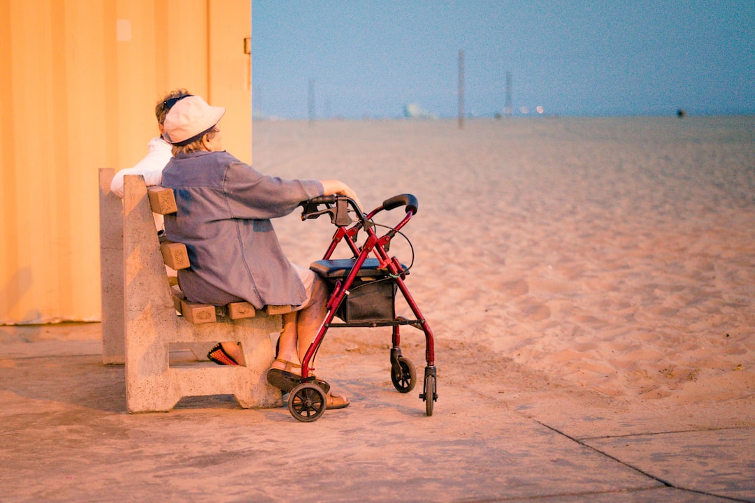 woman in gray dress shirt and white hat sitting on brown wooden bench near body of water